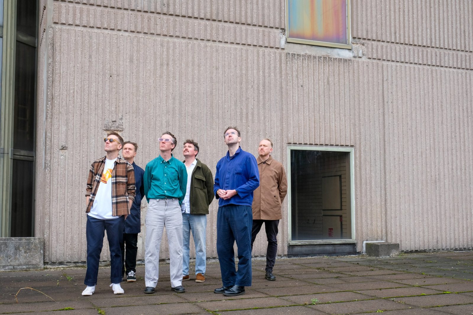 Dutch Uncles standing in front of a concrete building, looking up